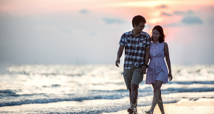 Un couple marchant main dans la main sur la plage au coucher du soleil, partageant un moment romantique