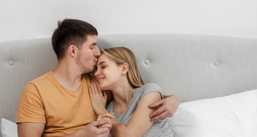 Couple partageant un moment tendre dans un lit avec des c&oelig;urs rouges