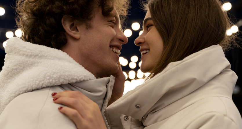 Couple complice se souriant sous des lumi&egrave;res romantiques en veste blanche