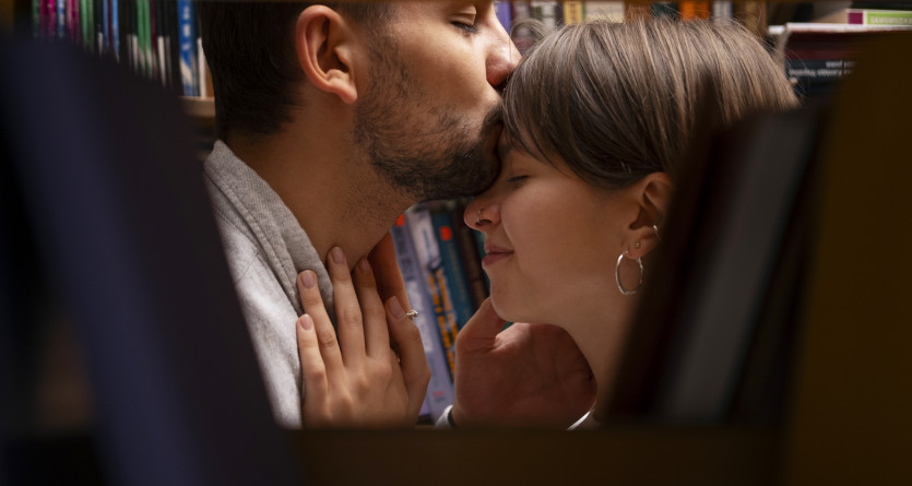Couple partageant un moment intime et complice, cach&eacute; entre des &eacute;tag&egrave;res de livres