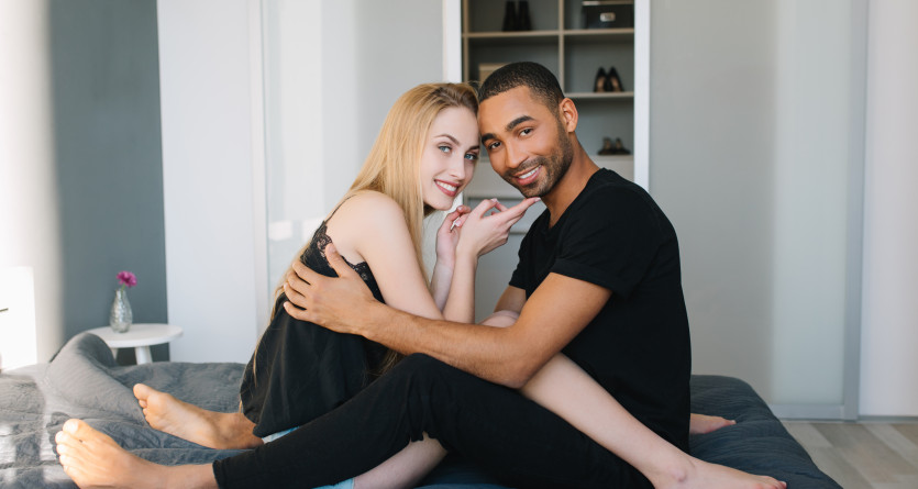Couple assis sur un lit, partageant un sourire complice dans une chambre romantique