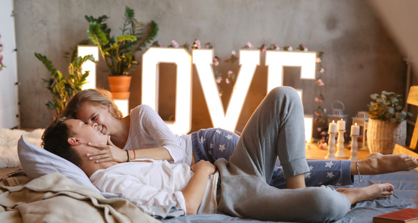 Couple souriant et enlac&eacute; dans une chambre romantique avec le mot "LOVE" en arri&egrave;re-plan