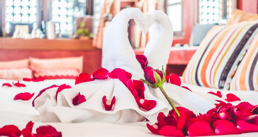 Serviettes en forme de cygnes entour&eacute;es de p&eacute;tales de roses sur un lit romantique