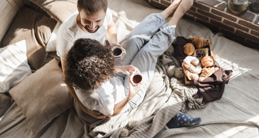 Couple partageant un petit d&eacute;jeuner cosy au lit, entour&eacute; de douce lumi&egrave;re matinale