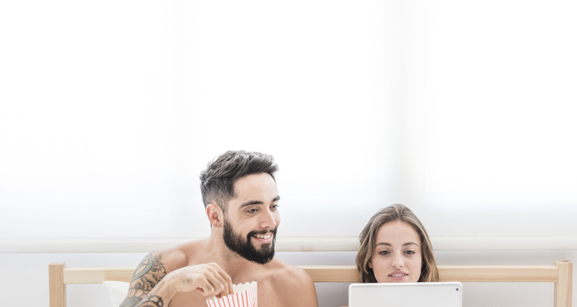 Couple allong&eacute; dans un lit, regardant un film sur une tablette et partageant du popcorn