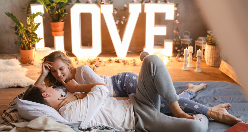 Un couple allong&eacute; dans une ambiance romantique, entour&eacute; de d&eacute;corations lumineuses et chaleureuses &eacute;voquant l&rsquo;amour.
