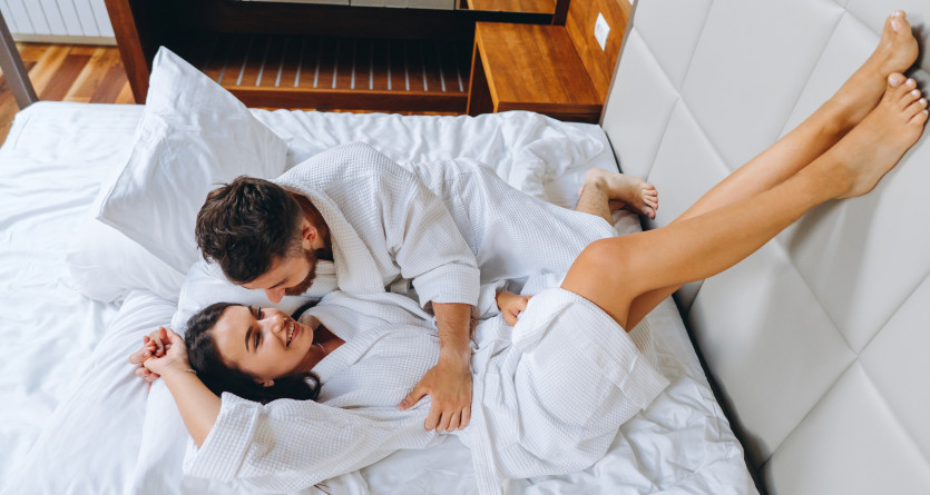 Un couple en peignoir partage un moment complice sur un lit confortable, parfait pour une escapade romantique en Love Room