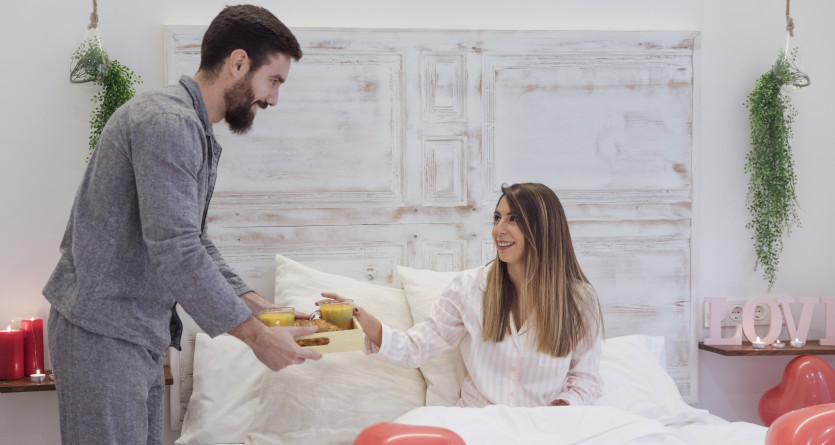 Un homme servant un petit-d&eacute;jeuner romantique &agrave; une femme dans une Love Room d&eacute;cor&eacute;e avec soin