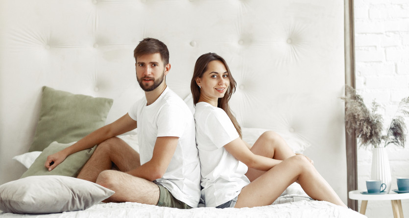 Un couple assis dos &agrave; dos sur un lit, partageant un moment de complicit&eacute; dans une chambre lumineuse et &eacute;l&eacute;gante