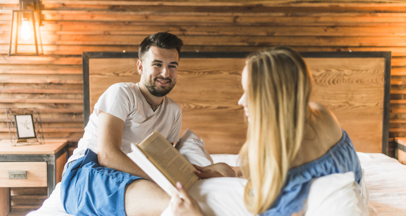 Couple partageant un moment de lecture complice dans une chambre chaleureuse avec des murs en bois
