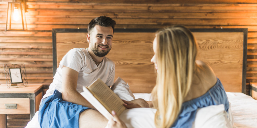 Couple partageant un moment de lecture complice dans une chambre chaleureuse avec des murs en bois