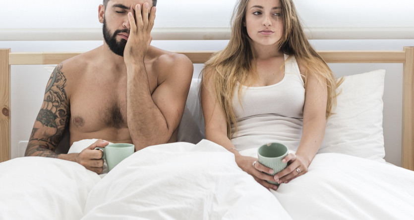 Un couple assis dans un lit, r&eacute;fl&eacute;chissant dans une ambiance de chambre lumineuse