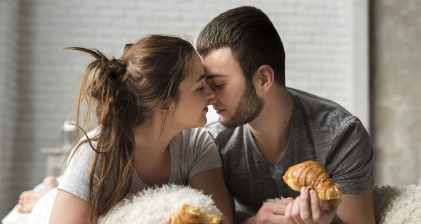 Un couple partageant un moment romantique avec un petit-d&eacute;jeuner au lit, dans une ambiance chaleureuse et intime