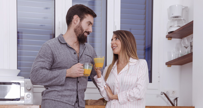 Un couple en pyjama partage un jus d&rsquo;orange dans une cuisine lumineuse, parfait pour un s&eacute;jour romantique dans une Love Room
