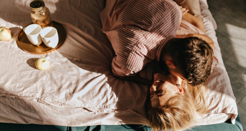 Un couple partage un moment complice et chaleureux sur un lit romantique baign&eacute; de lumi&egrave;re naturelle