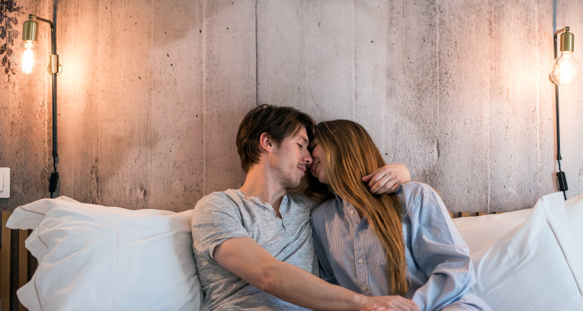 Un couple partage un moment tendre dans une chambre chaleureuse &agrave; l&rsquo;&eacute;clairage tamis&eacute;