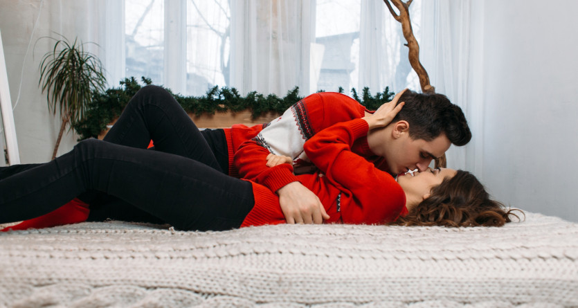 Un couple partage un baiser tendre dans une ambiance cosy et festive, v&ecirc;tus de pulls rouges assortis