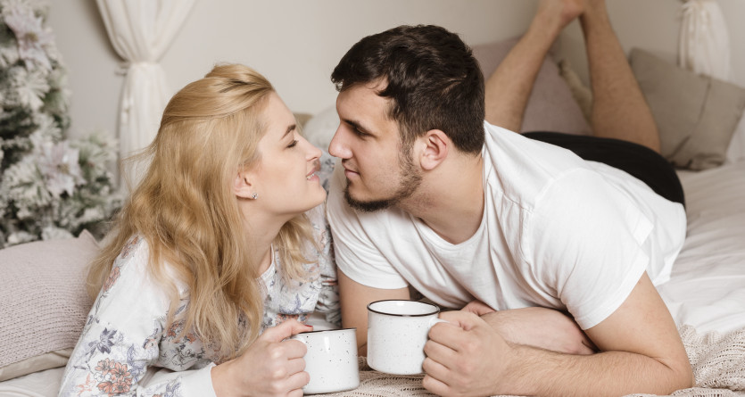 Couple amoureux partageant un moment de complicit&eacute; avec des tasses dans une chambre chaleureuse
