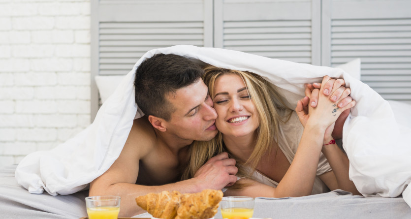 Couple partageant un moment romantique au lit avec un petit-d&eacute;jeuner dans une Love Room