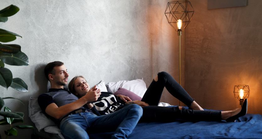 Un couple allong&eacute; sur un lit dans une chambre moderne, profitant d&rsquo;un moment de d&eacute;tente