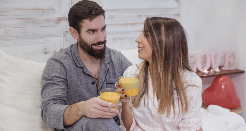 Un couple en pyjama trinquant avec des jus de fruits dans une chambre romantique d&eacute;cor&eacute;e avec des touches d&rsquo;amour