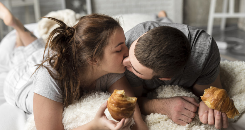 Couple s&rsquo;embrassant tendrement tout en partageant un petit-d&eacute;jeuner au lit