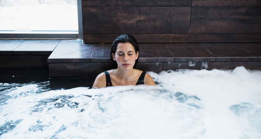 Femme d&eacute;tendue dans un jacuzzi moussant avec vue sur la neige, une Secret Room d'hiver apaisante.