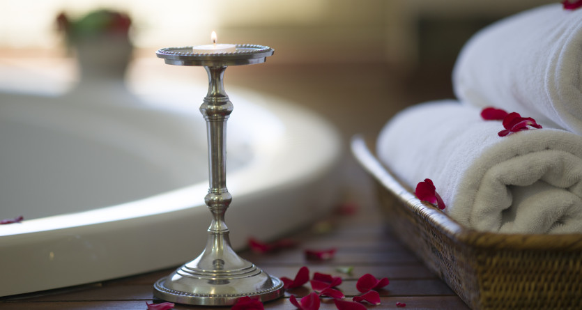 Bougie allum&eacute;e et p&eacute;tales de rose pr&egrave;s d'un jacuzzi dans une chambre romantique