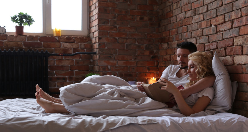 Couple lisant ensemble dans un lit confortable avec un mur en briques comme fond