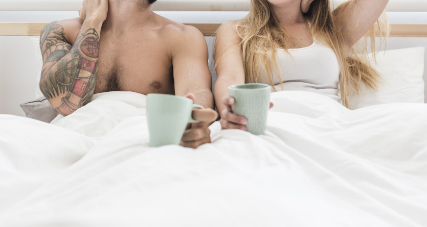 Couple souriant, profitant d'un caf&eacute; au lit dans une chambre lumineuse