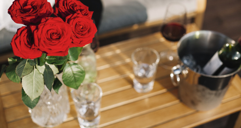 Bouquet de roses rouges vives sur une table en bois avec du vin et des verres