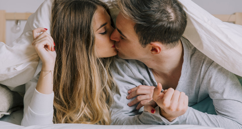 Jeune couple &eacute;changeant un baiser passionn&eacute; sous un drap blanc