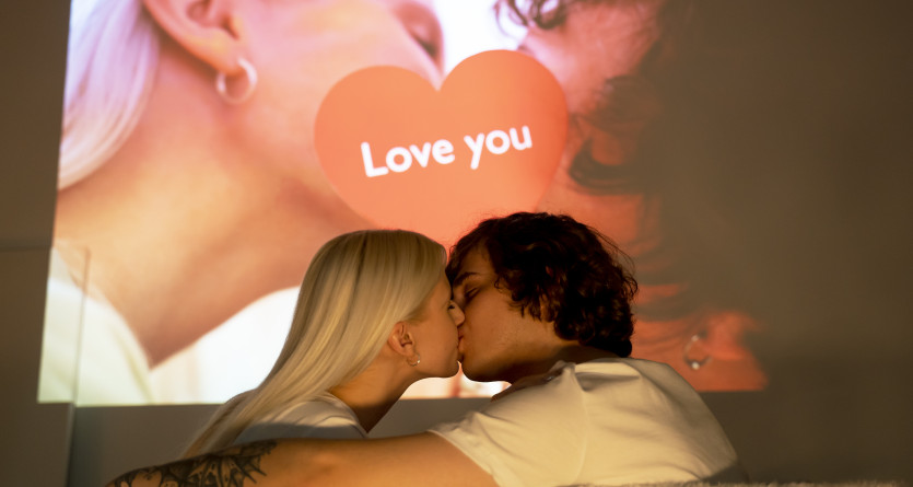 Couple s'embrassant sous la lumi&egrave;re d'un projecteur affichant un message d'amour