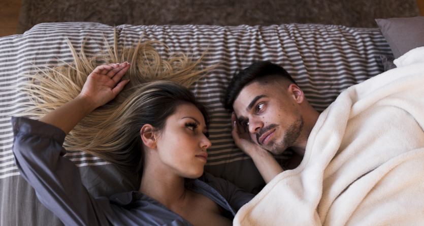Couple allong&eacute; face &agrave; face, partageant un regard intime sous une couverture douillette
