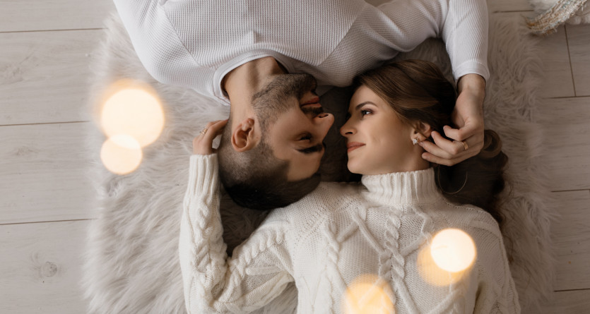 Couple en tenue d'hiver se regardant amoureusement, allong&eacute;s sur un tapis doux