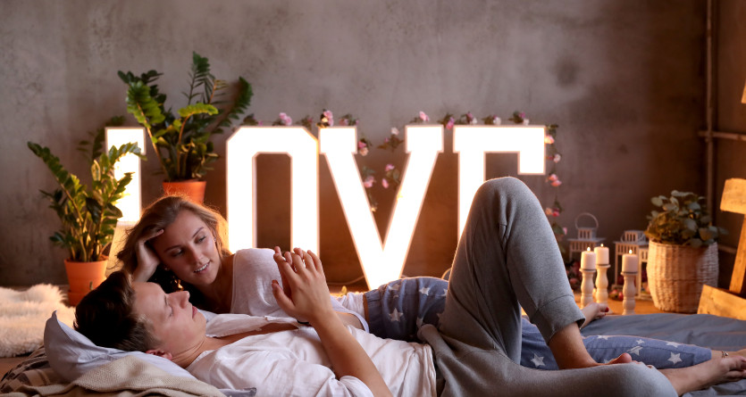 Couple d&eacute;tendu dans une chambre romantique d&eacute;cor&eacute;e avec des lettres LOVE illumin&eacute;es