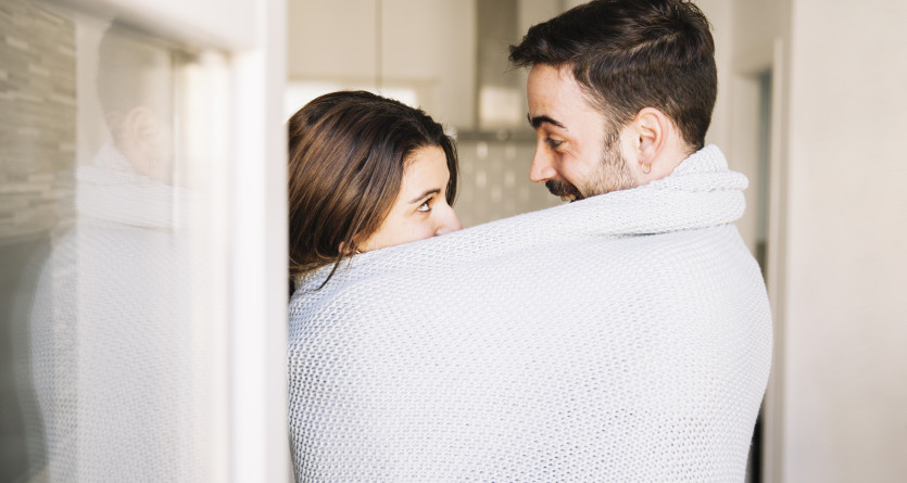 Couple &eacute;changeant un regard intime sous une couverture douillette dans un int&eacute;rieur moderne