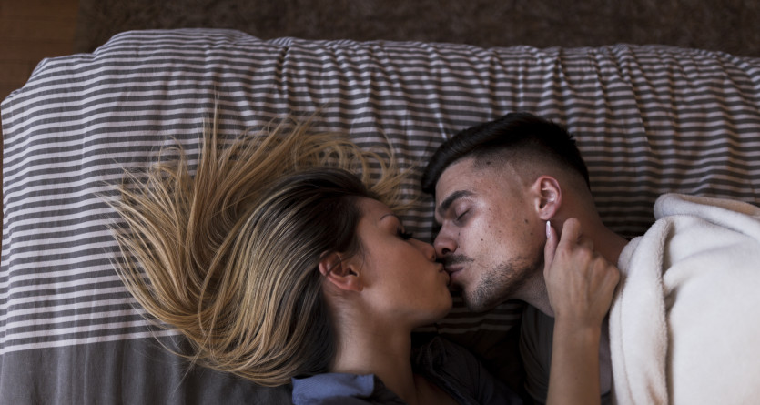 Couple s'embrassant tendrement sur un lit &agrave; rayures dans une ambiance intime