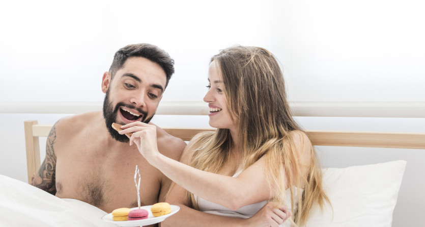 Femme souriante donnant un biscuit &agrave; son compagnon au lit, c&eacute;l&eacute;brant un moment intime