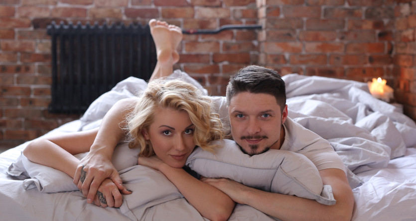Couple d&eacute;tendu posant joyeusement dans leur lit, ambiance chaleureuse et intime