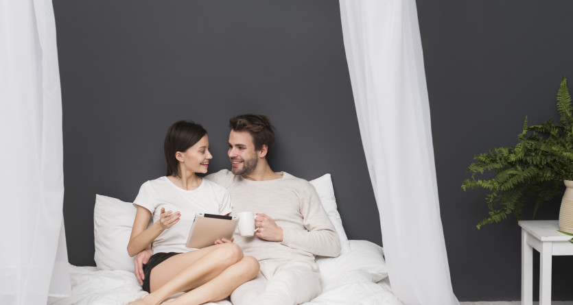 Couple souriant utilisant une tablette num&eacute;rique au lit