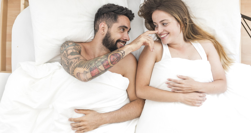 Couple souriant se touchant le nez dans un lit douillet