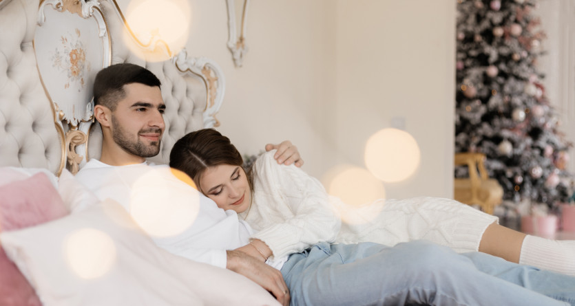 Couple d&eacute;tendu dans un lit luxueux avec un arbre de No&euml;l en arri&egrave;re-plan