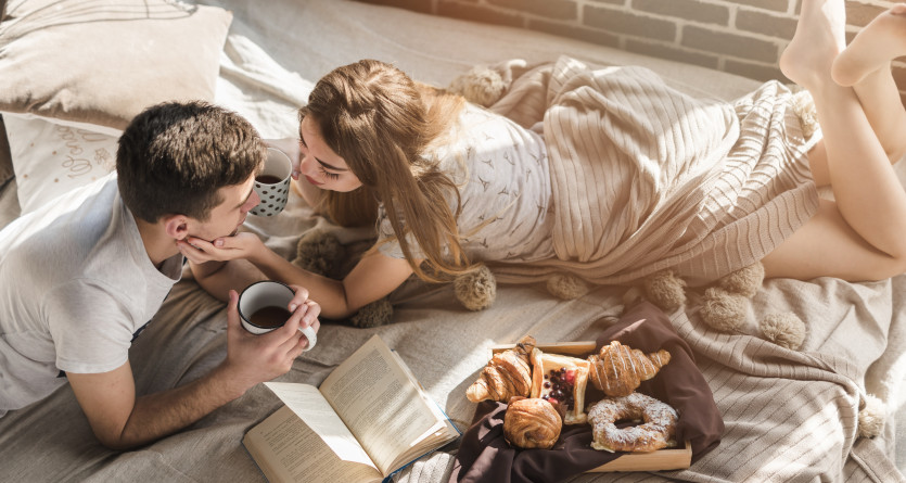 Couple profitant d'un petit-d&eacute;jeuner romantique au lit dans une chambre ensoleill&eacute;e