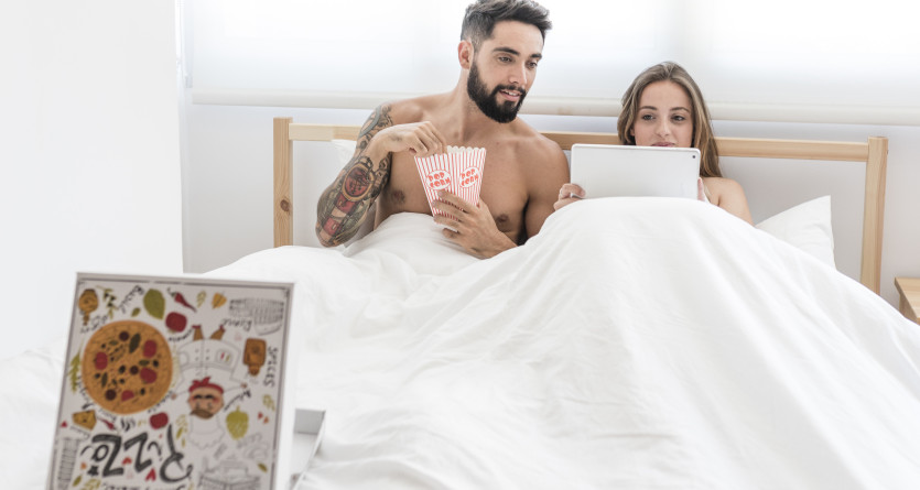 Couple regardant une tablette et mangeant du popcorn au lit dans une chambre romantique