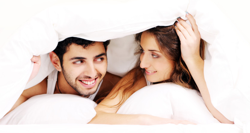Couple souriant sous une couette, partageant un moment intime dans une Love Room