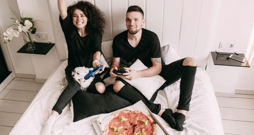 Couple souriant jouant &agrave; des jeux vid&eacute;o avec une pizza dans une Secret Room