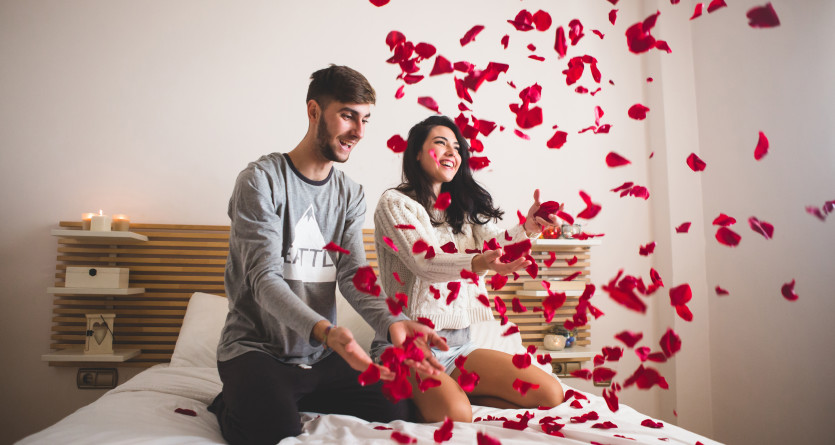 Couple jouant avec des p&eacute;tales de rose dans une chambre romantique