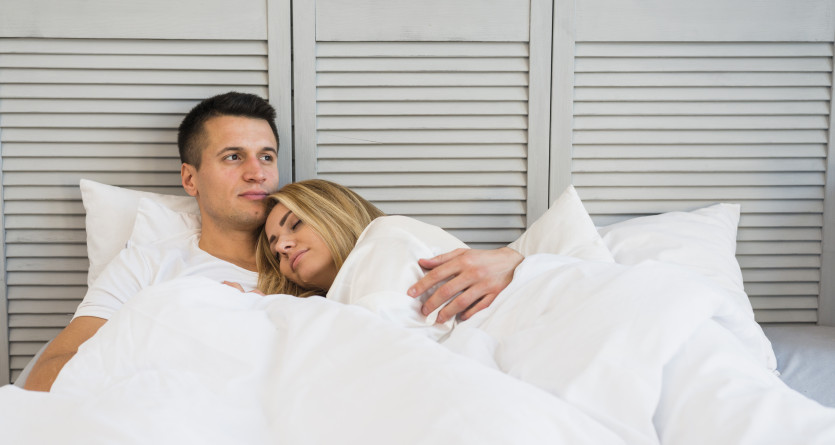 Couple allong&eacute;, partageant un moment de tendresse dans un lit cosy