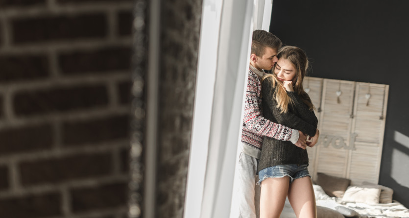 Couple partageant un instant de tendresse, enlac&eacute; pr&egrave;s d'une fen&ecirc;tre